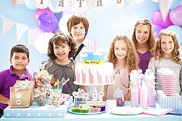 Children smiling near cake and gifts at birthday party