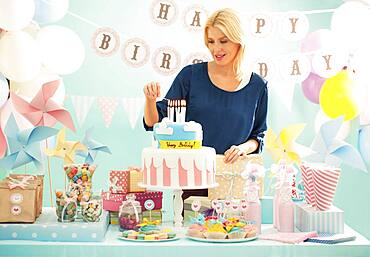 Woman lighting candles on birthday cake at party