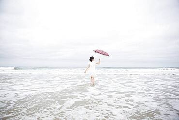 Woman wading with umbrella on beach