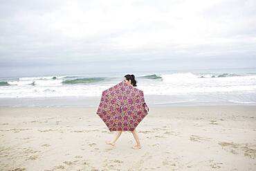 Woman walking with umbrella on beach