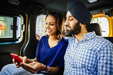 Indian couple using cell phone in taxi