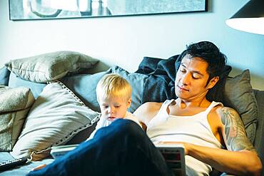 Father and son reading on sofa in living room