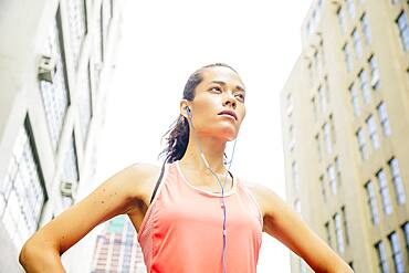 Mixed race athlete listening to earbuds in city