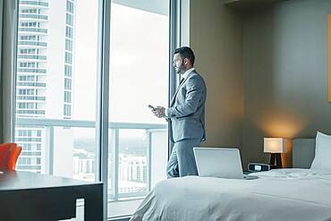 Businessman using cell phone at hotel window