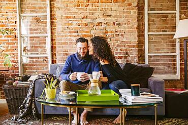 Couple drinking coffee on sofa in living room