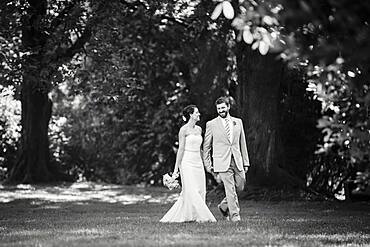 Caucasian bride and groom walking in grass