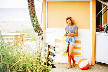 Mixed race teenager using cell phone on beach