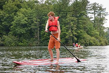 Caucasian teenage boy rowing paddleboat in lake