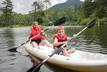 Caucasian mother and son rowing canoe in lake