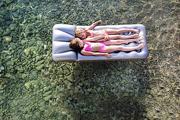 Caucasian girls floating on raft in lake