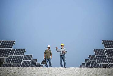 Caucasian technicians talking near solar panels