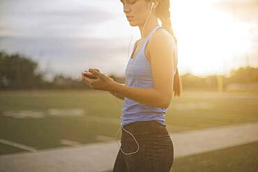 Mixed race athlete listening to mp3 player on sports field