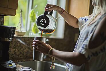 Caucasian woman pouring cup of coffee in kitchen