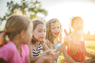 Girls eating flavored ice in sunny field