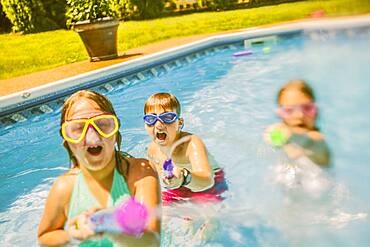 Caucasian children playing with squirt guns in swimming pool