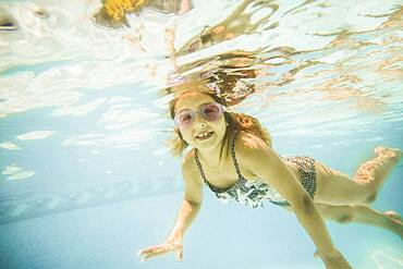 Caucasian girl swimming underwater in swimming pool