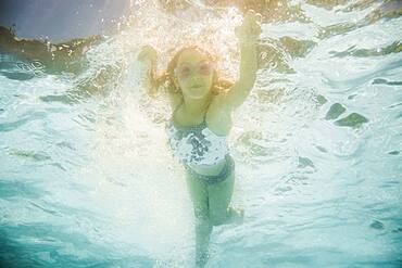 Caucasian girl swimming underwater in swimming pool