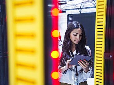 Mixed race technician using digital tablet in server room