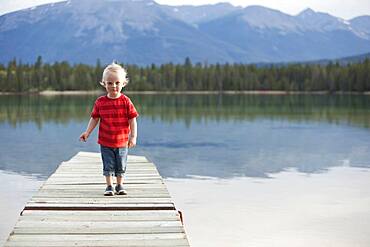 Caucasian boy walking on dock over remote lake