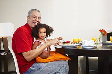 Grandfather and granddaughter eating breakfast at table