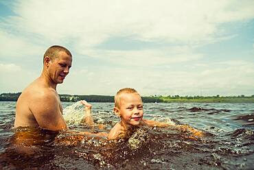 Caucasian father and son swimming in lake