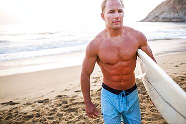 Caucasian surfer carrying surfboard on beach