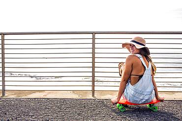 Caucasian woman sitting on skateboard at beach