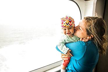 Caucasian mother kissing baby daughter at window