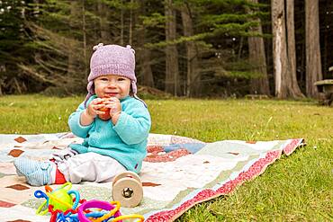 Caucasian baby girl sitting on blanket in grass