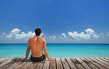 Caucasian man sitting on wooden dock at ocean