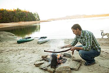 Man building campfire at lake