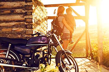 Mother holding son near motorcycle on patio