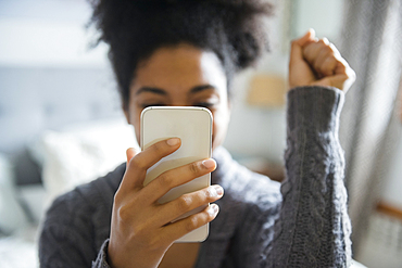 African American woman celebrating while texting on cell phone