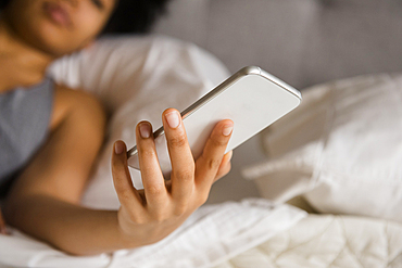 African American woman laying on bed texting on cell phone