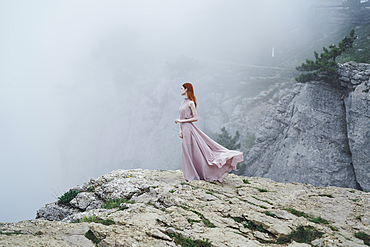 Caucasian woman wearing dress on rock in fog