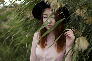 Pensive Asian woman standing in field of tall grass