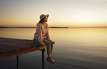 Caucasian woman sitting on dock of lake admiring sunset