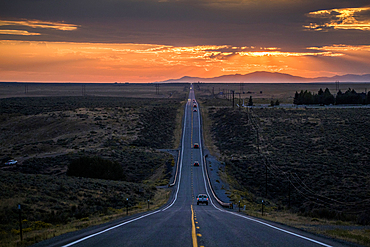 Cars driving on remote road at sunset