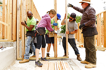 Volunteers lifting framed wall at construction site