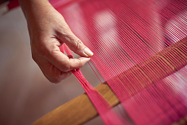 Hand of Hispanic woman weaving fabric on loom