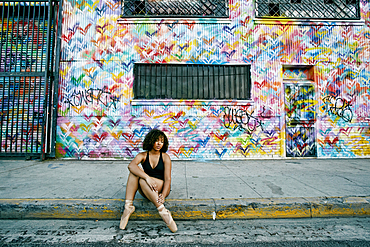 Mixed race ballet dancer sitting on curb rubbing leg