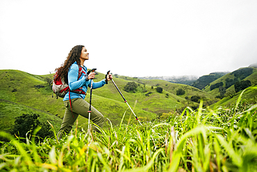 Smiling mixed race woman hiking with walking sticks