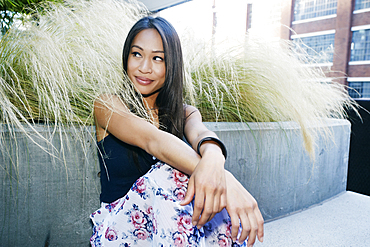 Smiling Asian woman sitting near foliage