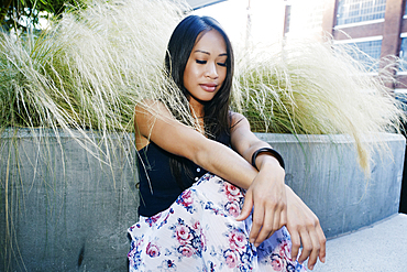 Pensive Asian woman sitting near foliage