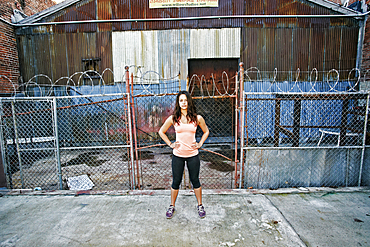 Confident mixed race woman standing on sidewalk near barbed-wire fence