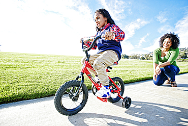 Mixed race mother watching daughter riding bicycle