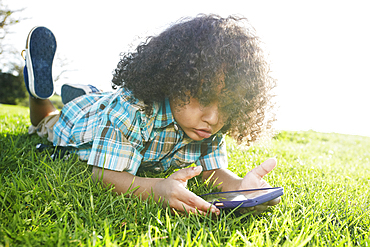 Mixed race boy laying in grass holding cell phone