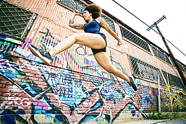 Hispanic woman running and jumping near graffiti wall