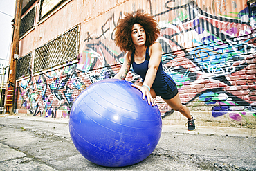 Hispanic woman balancing on fitness ball near graffiti wall