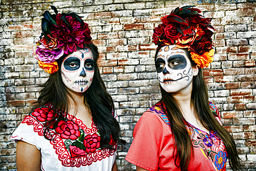 Women near brick wall wearing skull face paint